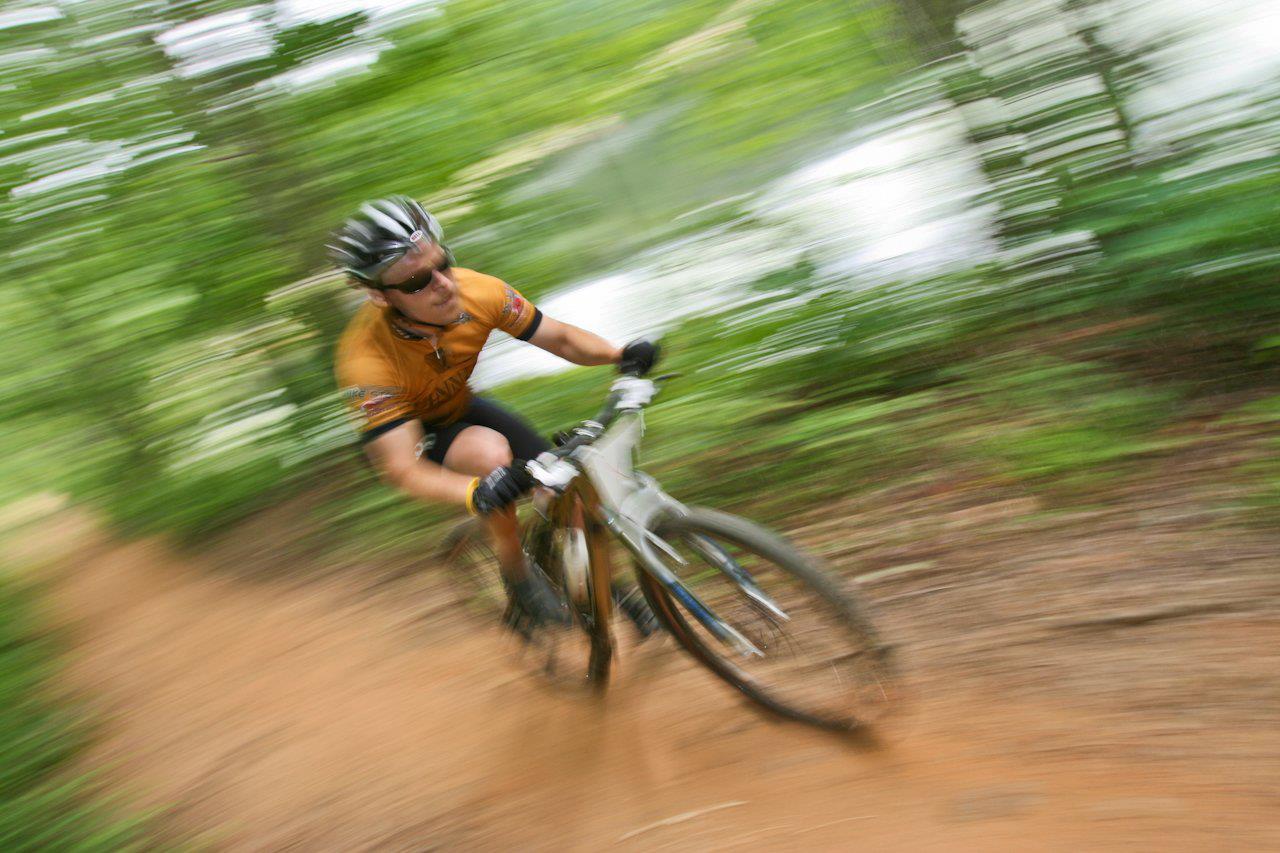 A man is riding a bike down a dirt trail in the woods.