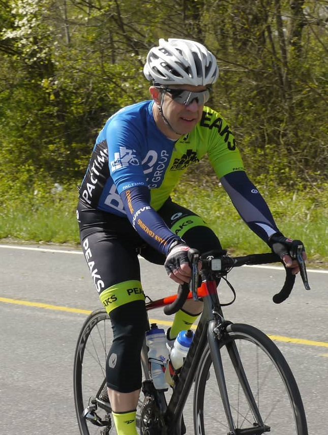 A man wearing a helmet and sunglasses is riding a bike on a road