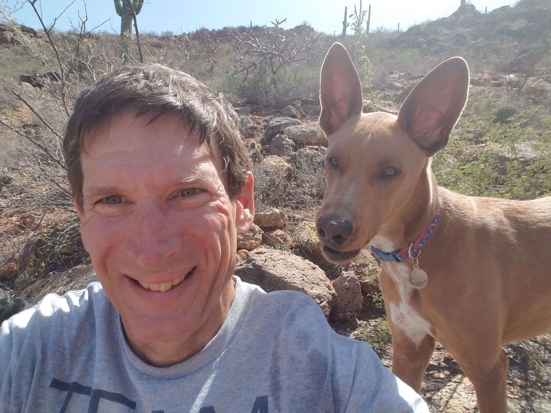 A man is taking a selfie with his dog in the desert.