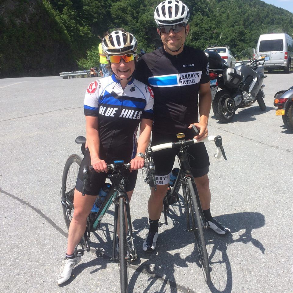 A man and a woman standing next to bicycles with one wearing a shirt that says rbe hills