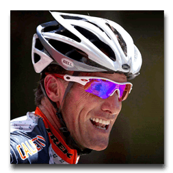 A man wearing a bell helmet and sunglasses smiles
