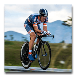 A man is riding a bike on a road with mountains in the background.