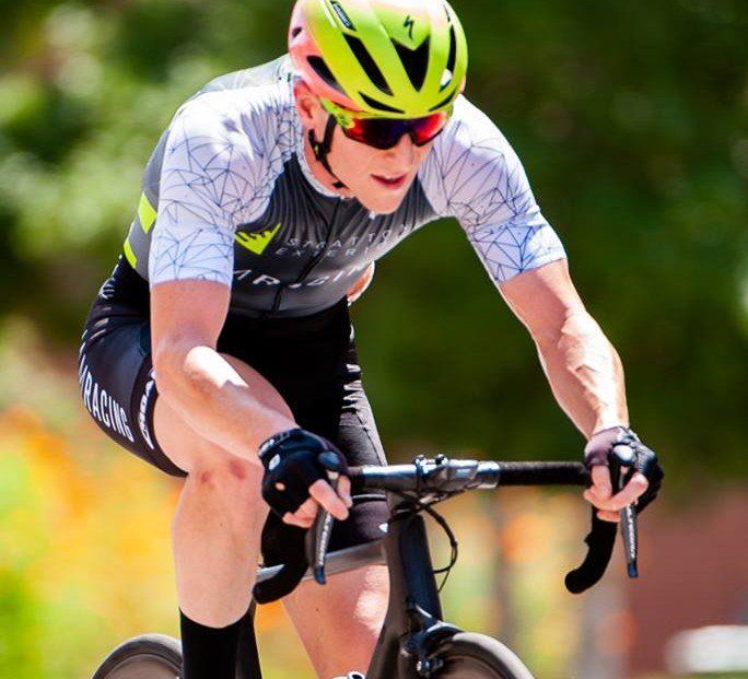 A man wearing a helmet and sunglasses is riding a bike