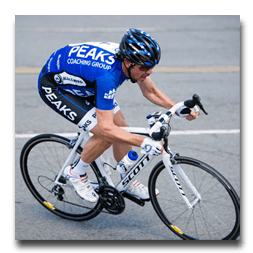 A man riding a bike with peaks coaching group on his shirt