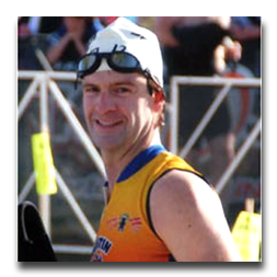 A man wearing a swim cap and goggles is smiling