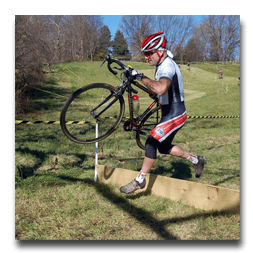 A man is jumping over a wooden fence while holding a bicycle