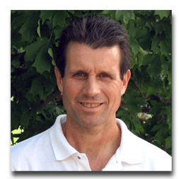 A man in a white shirt is smiling in front of a tree