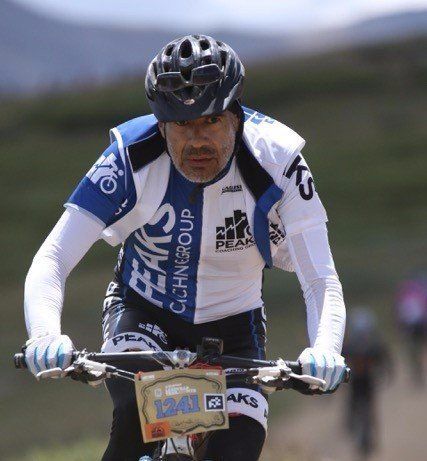 A man wearing a helmet and a shirt that says peaks is riding a bike