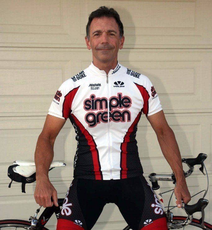 A man wearing a simple green jersey stands next to a bicycle