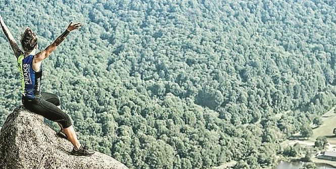 A woman is sitting on top of a rock with her arms in the air.