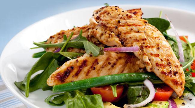 A white plate topped with grilled chicken and vegetables.