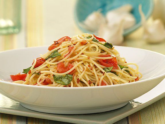 A bowl of spaghetti with tomatoes and basil on a table.