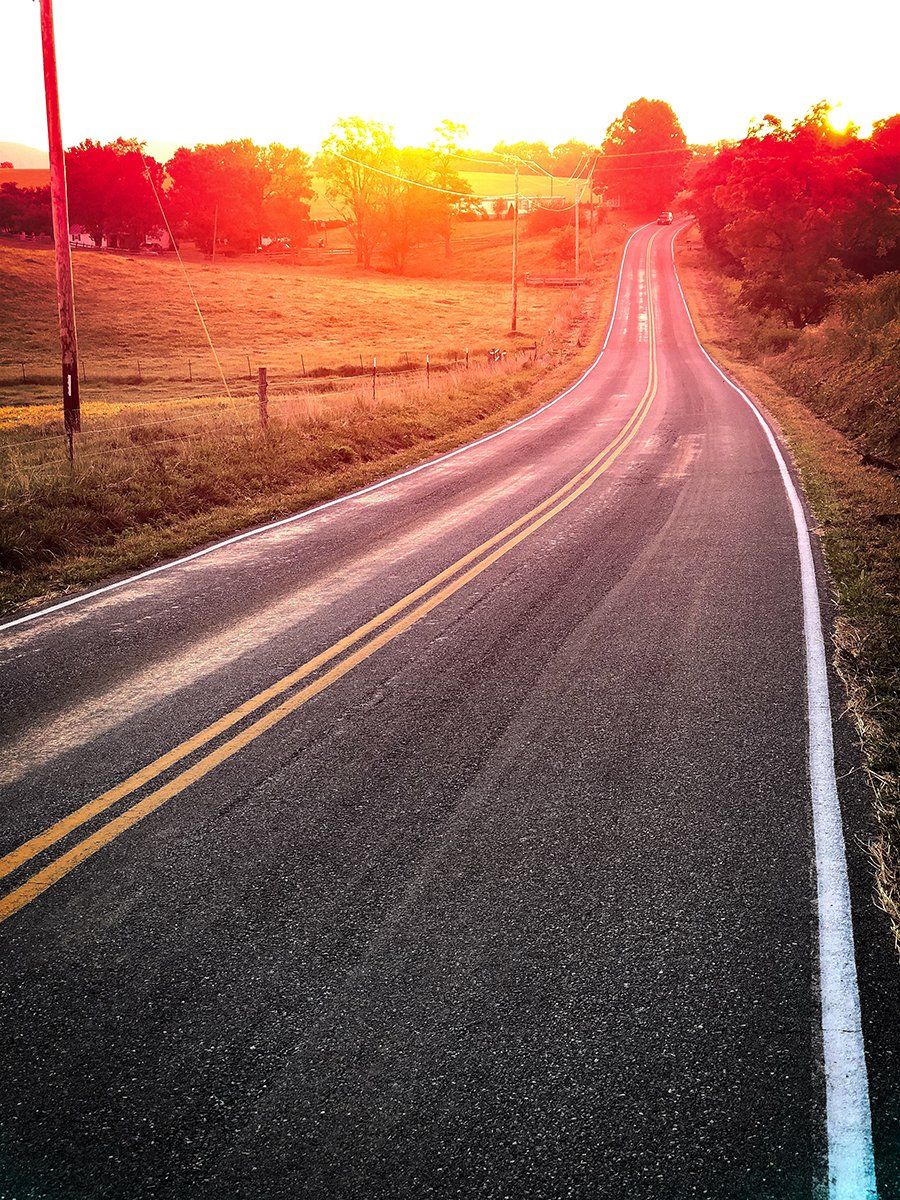 A road that is going through a field with a sunset in the background
