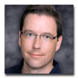 A man wearing glasses and a blue shirt is smiling for the camera.