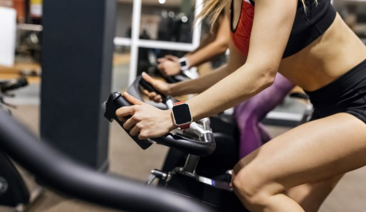 Two women are riding exercise bikes in a gym.