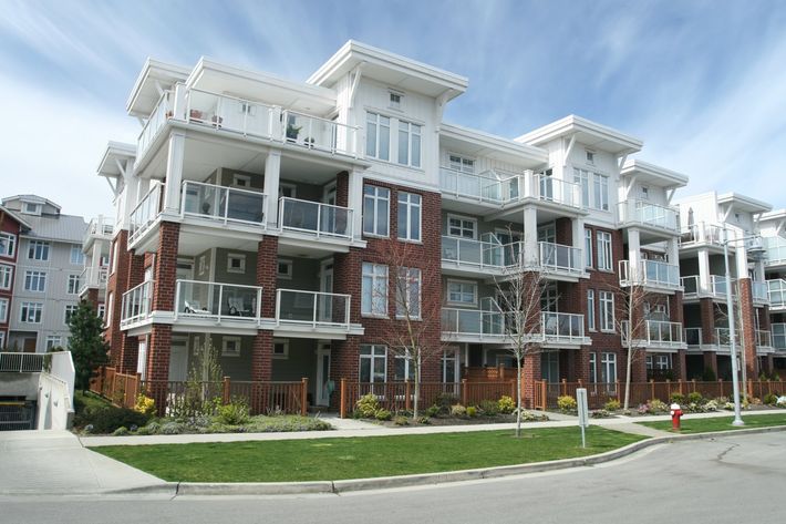 Modern red-brick apartment building with white balconies and landscaped front lawn on a street corner