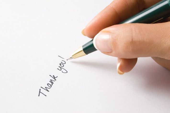 Hand writing “Thank you” with a green pen on white paper