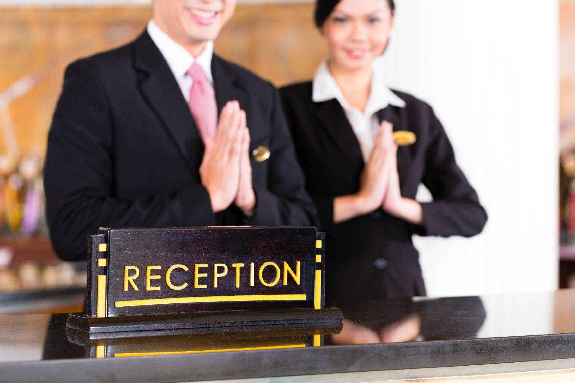 A man and a woman are standing at a hospitality reception desk.