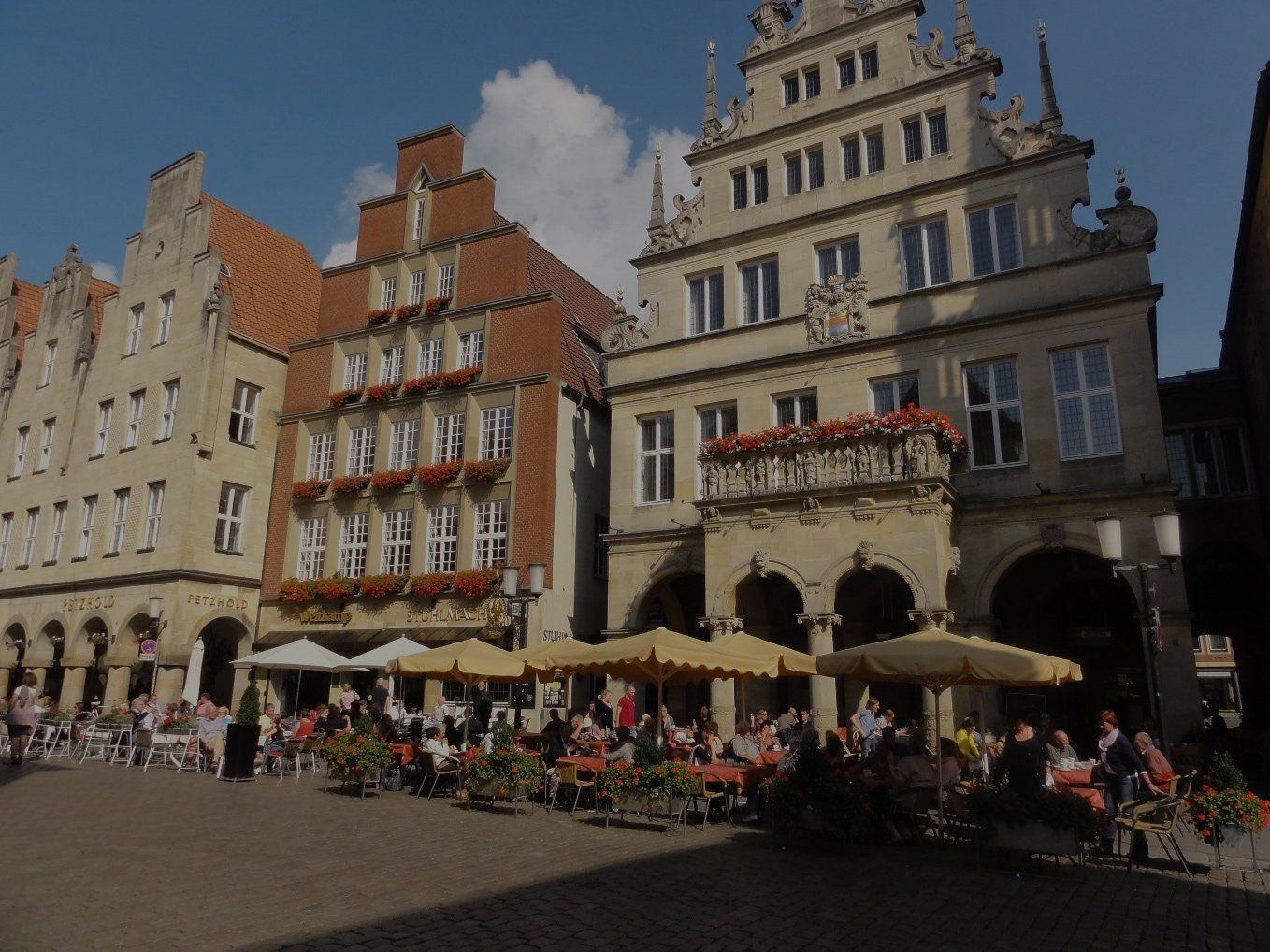 Eine Gruppe von Menschen sitzt unter Sonnenschirmen vor einem Gebäude
