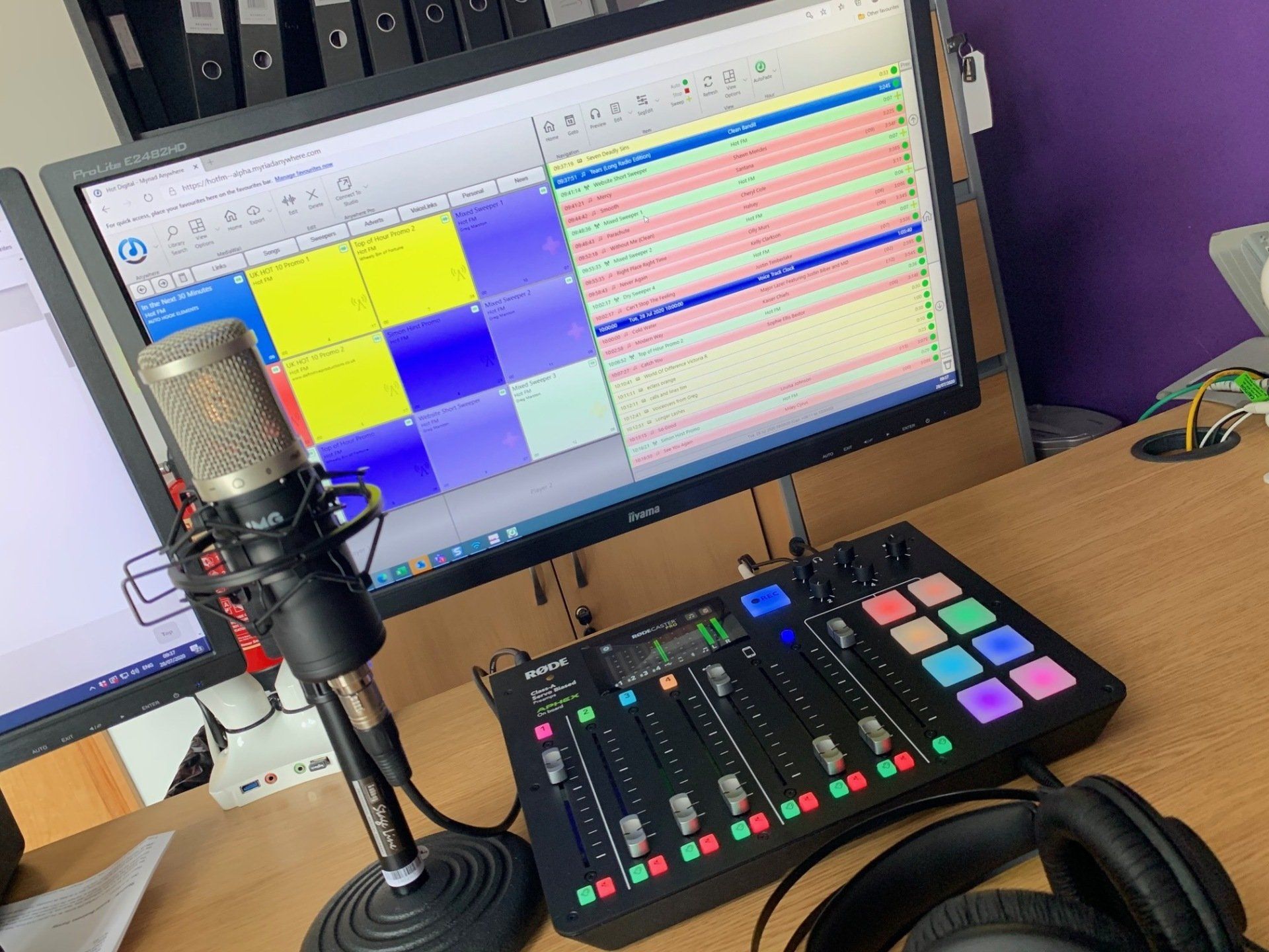 A microphone and headphones are on a desk in front of a computer monitor.