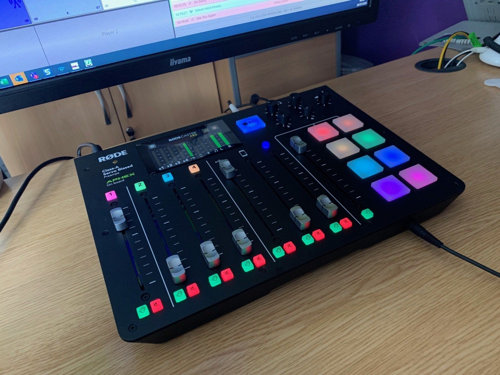 A mixer is sitting on a wooden table next to a computer monitor.