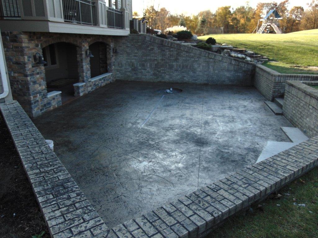A large stamped concrete patio with a stone wall and stairs