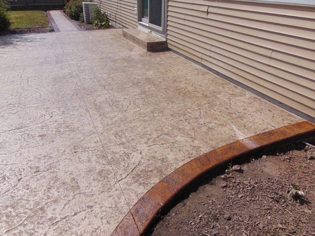 A concrete walkway with a brown border is in front of a house