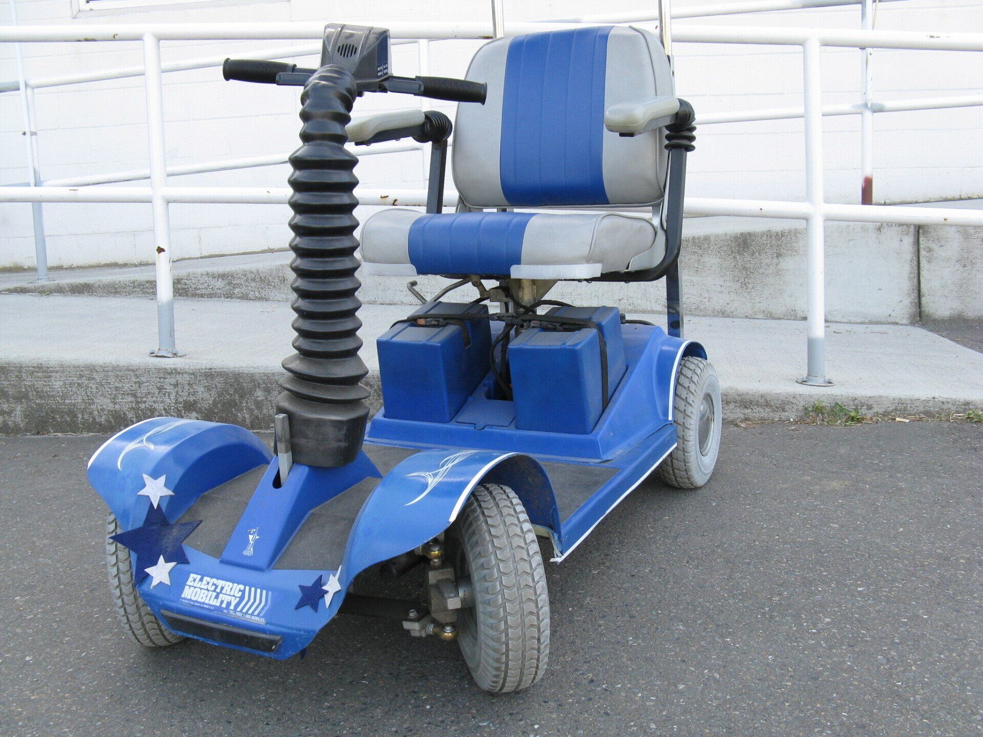 Blue and white mobility scooter with star decorations, parked on asphalt.