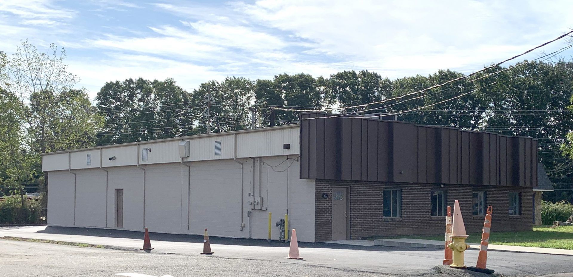 A commercial building with brown and white walls, a row of trees, and traffic cones.