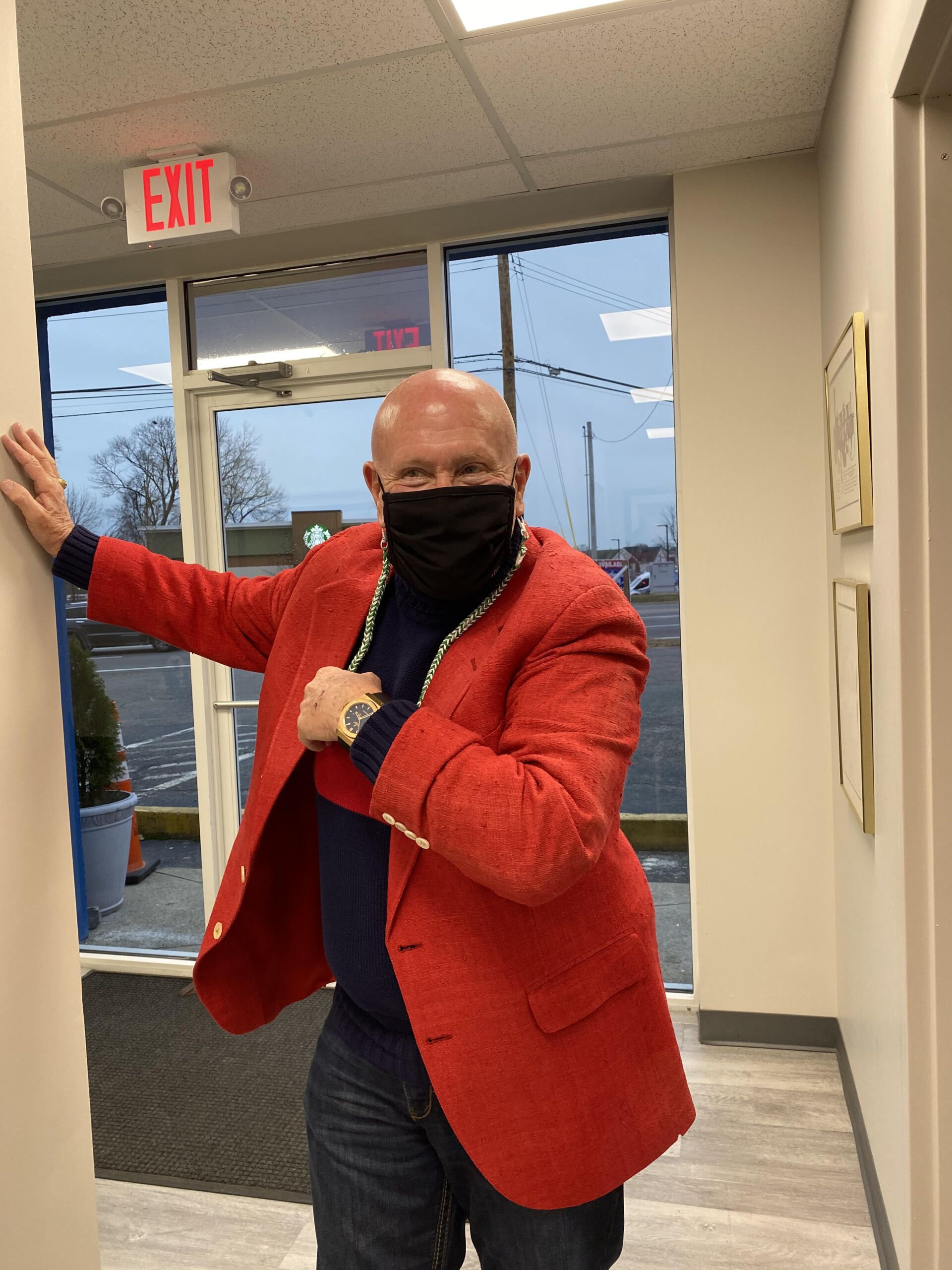 Man in red blazer and mask dances in a hallway.