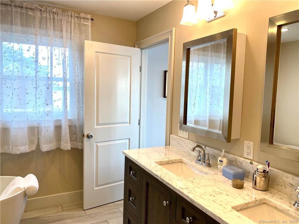 Bathroom with double sinks, white countertop, dark cabinets, and a sheer curtain over the window.