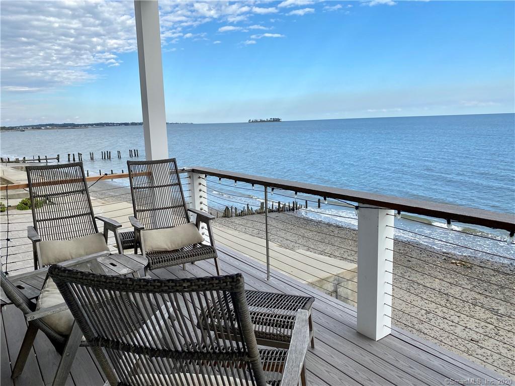 Deck with chairs overlooking a beach and ocean on a sunny day.
