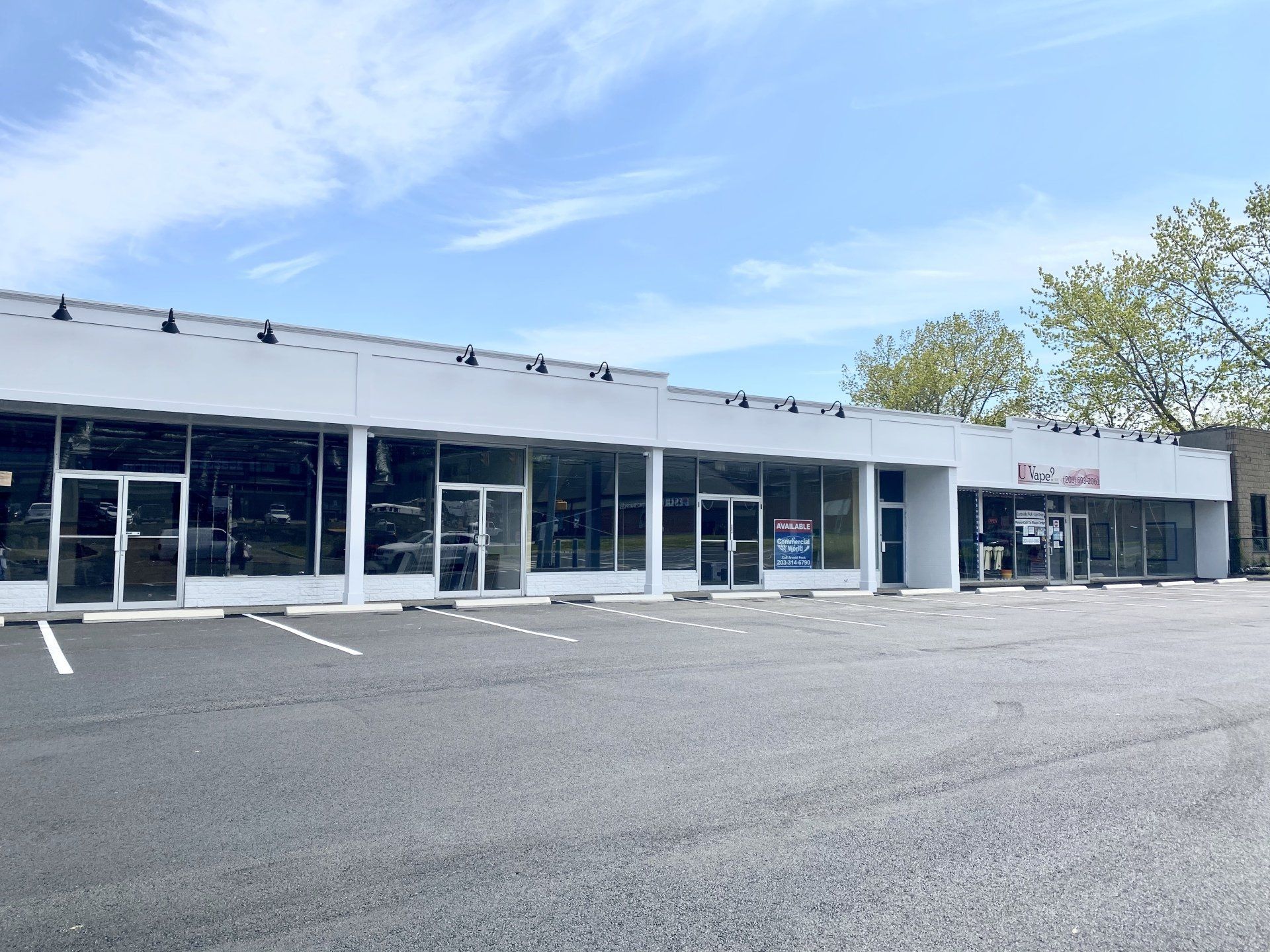 A long, white, single-story commercial building with large glass windows and doors. Blue sky above.