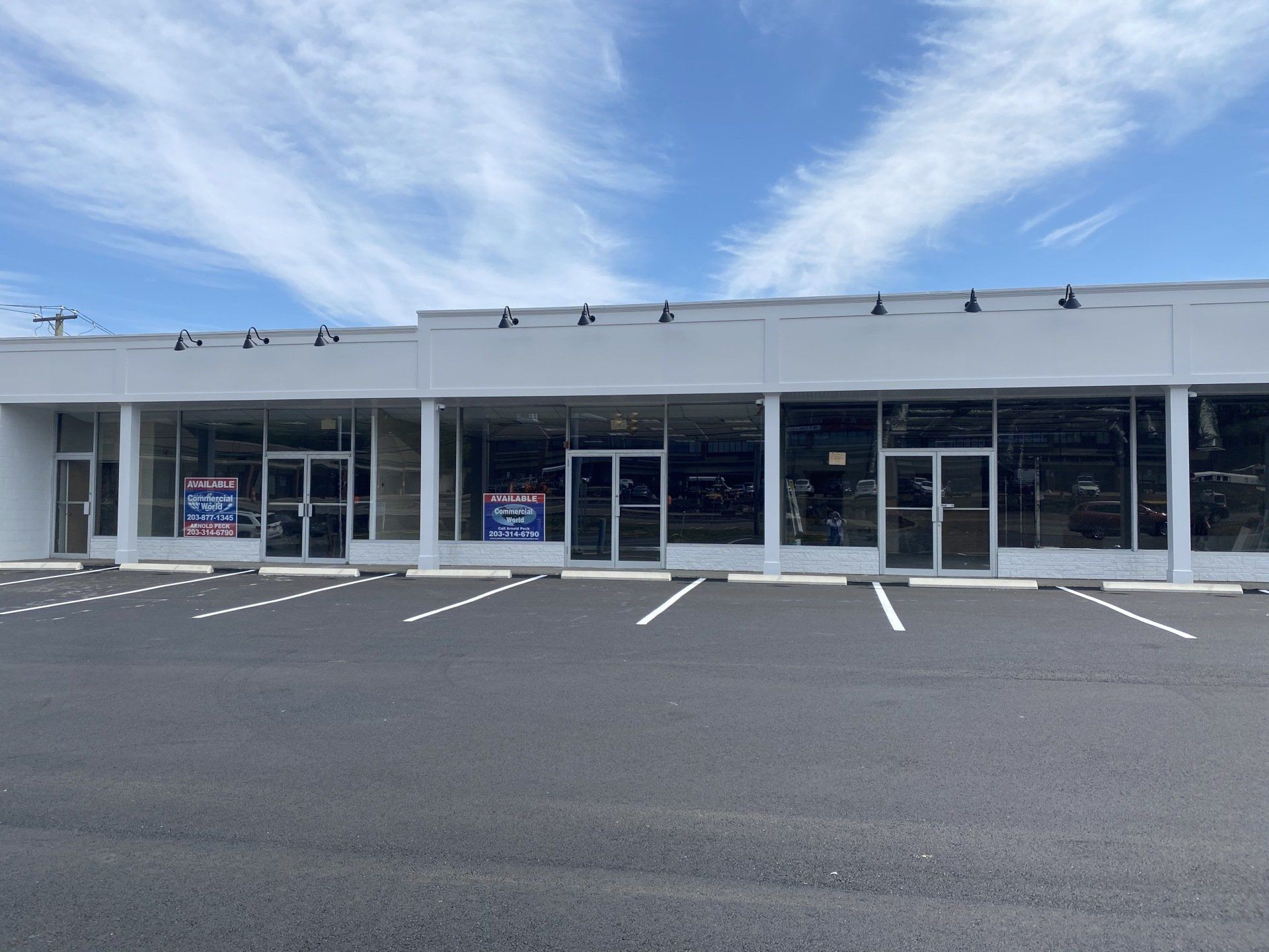 White storefront with glass windows and doors, on a sunny day. Empty parking lot.