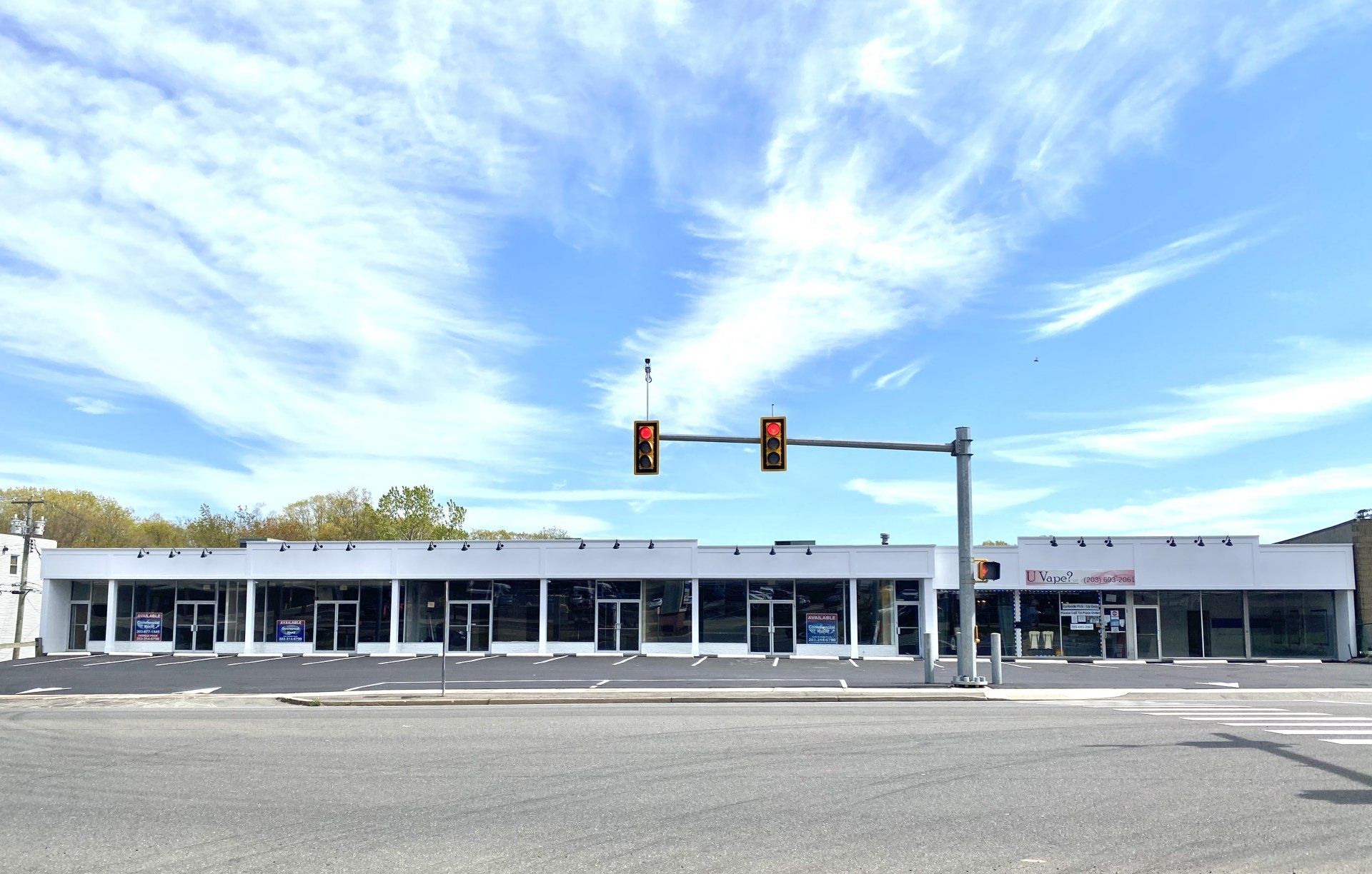 A long, white, single-story commercial building under a blue sky, with traffic lights in front.