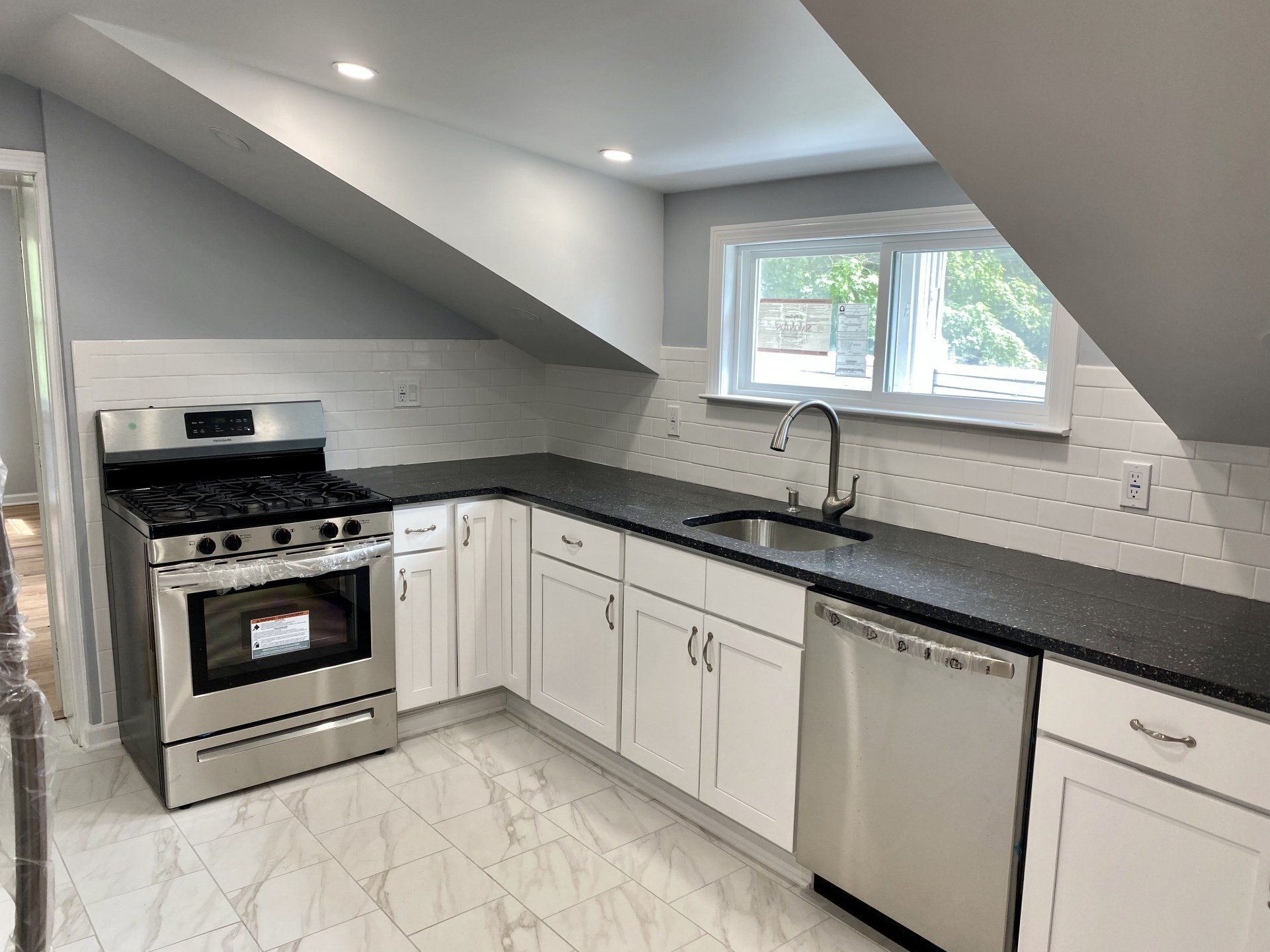 Modern kitchen with stainless steel appliances, white cabinets, dark countertop, and angled ceiling.