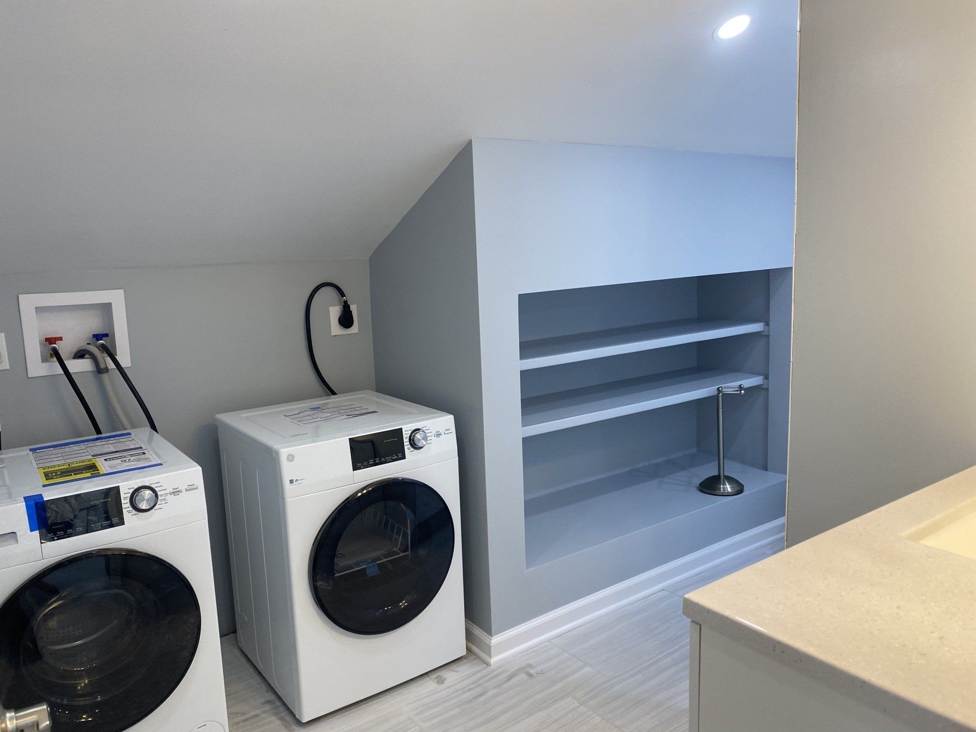 Laundry room with a washer, dryer, and built-in shelving, all painted gray.