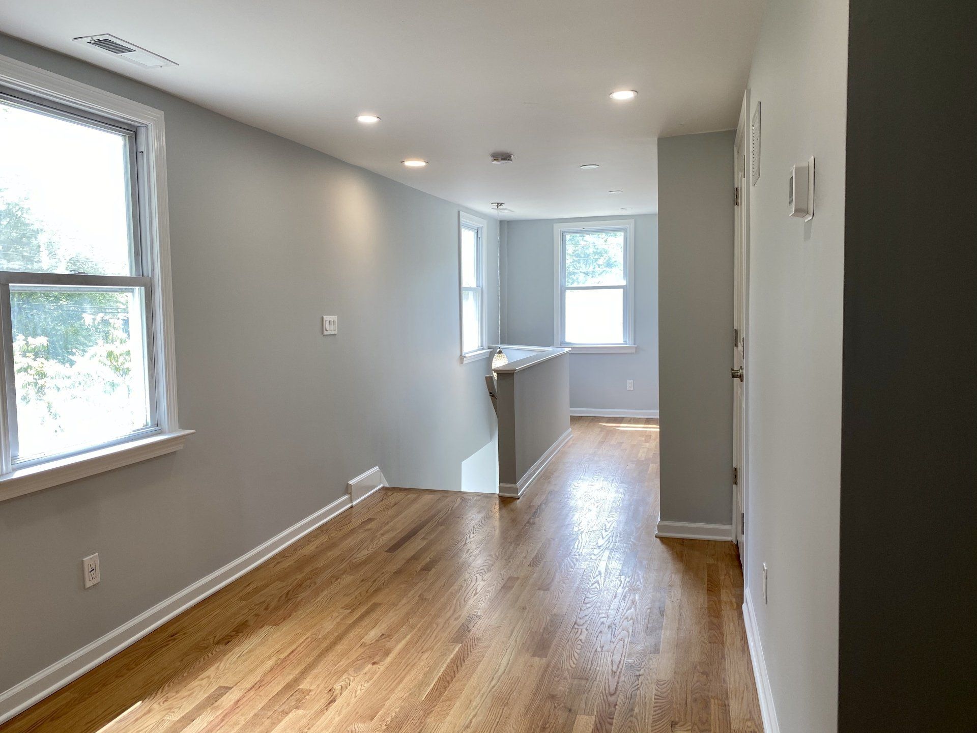 Empty hallway with hardwood floors, light gray walls, and natural light from windows.