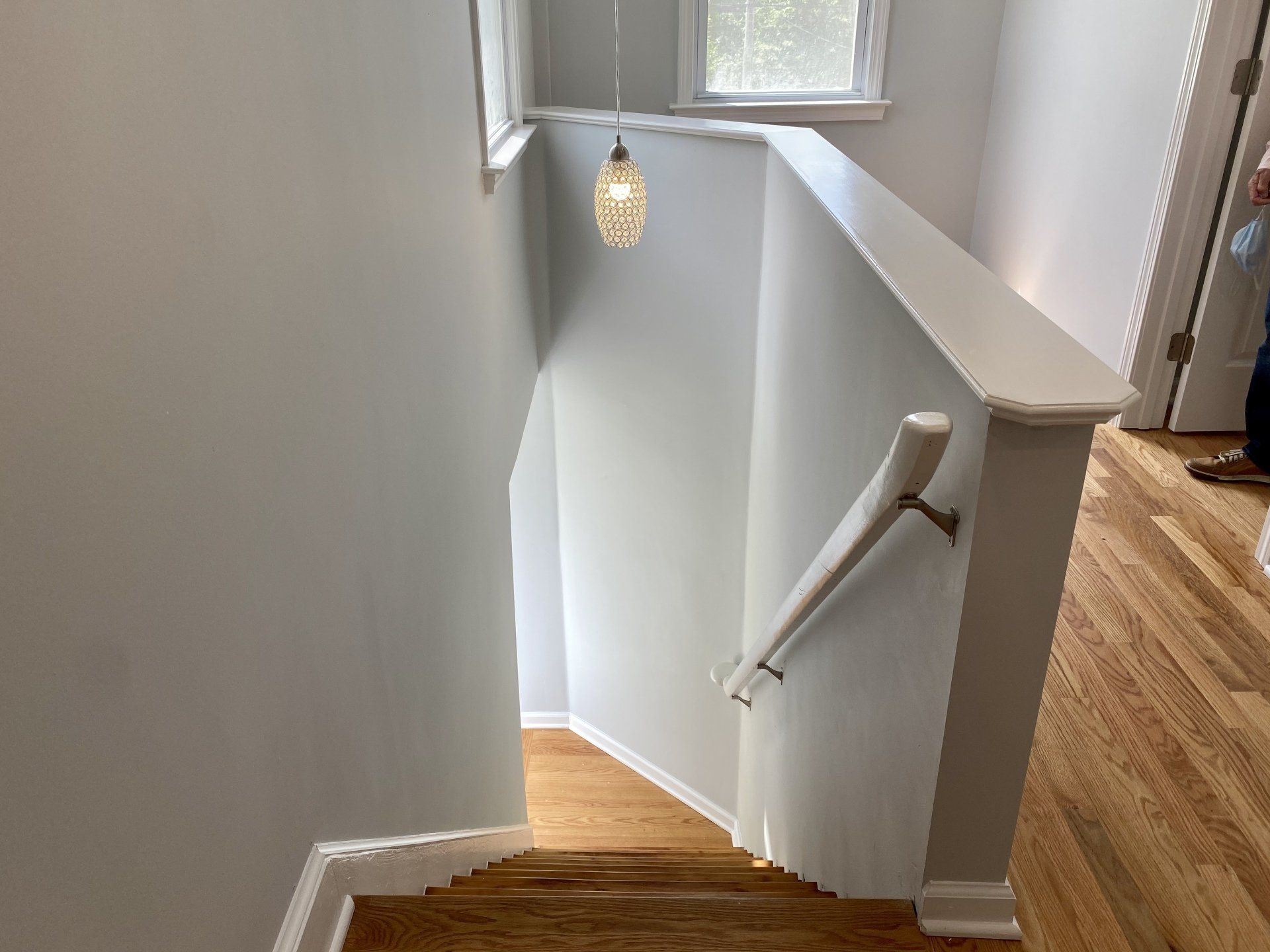 Stairwell with wooden steps and white handrail; light gray walls, a window, and a hanging light fixture.
