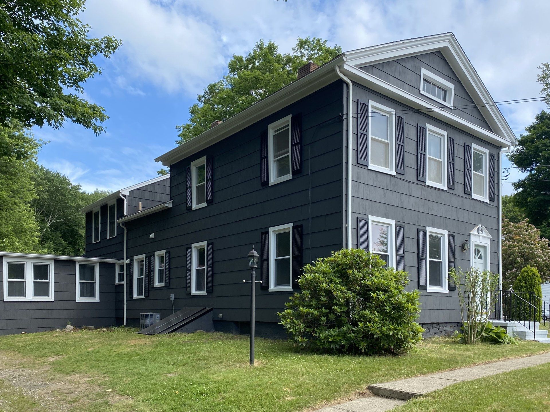 Dark gray house with white trim, black shutters, and a lawn.