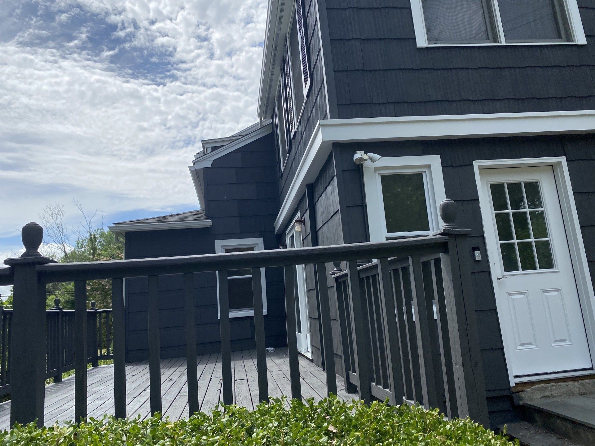 Dark gray house with white trim, deck, and door; partly cloudy sky.