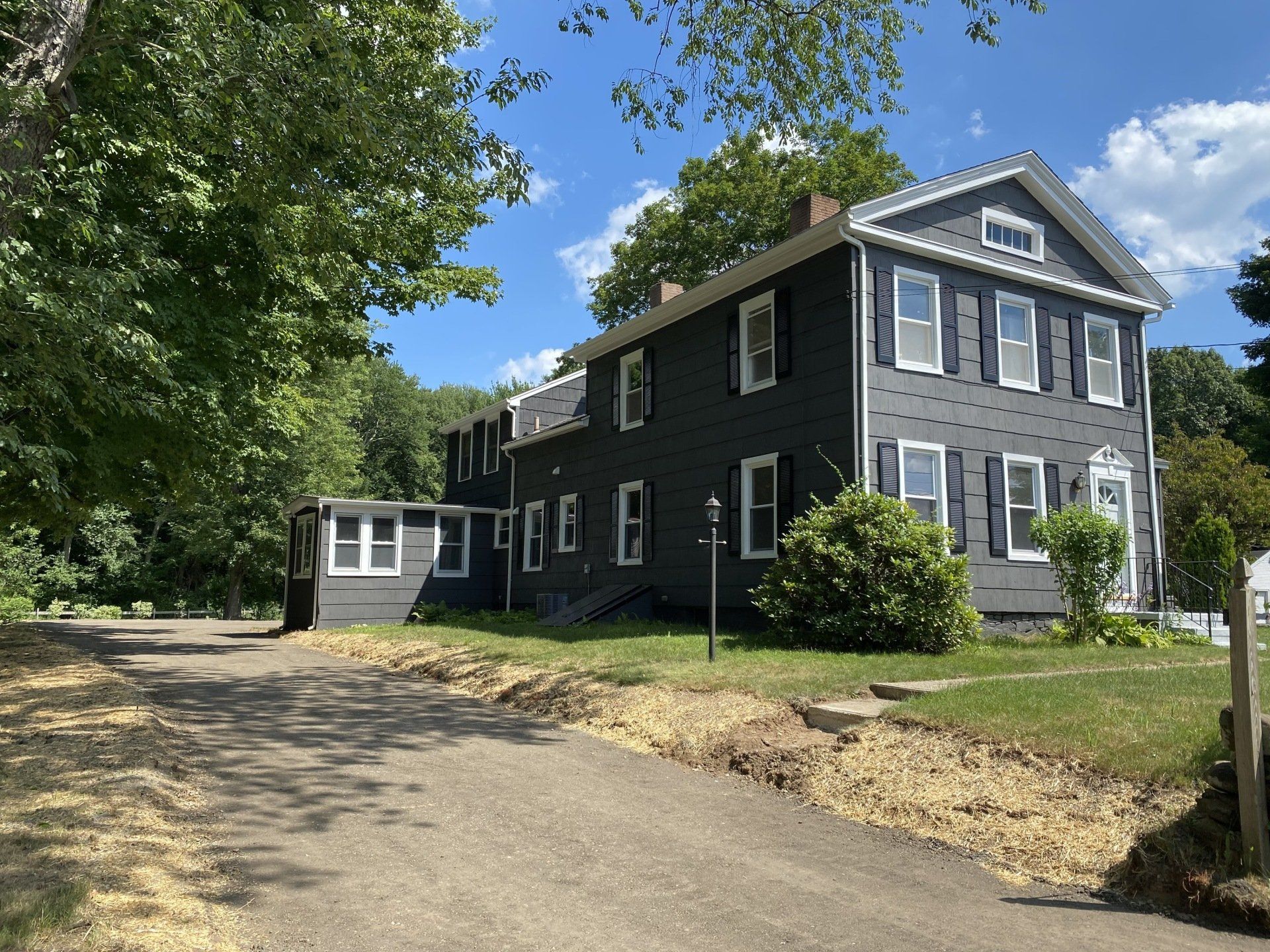 Dark grey house with black shutters, white trim, and a gravel driveway on a sunny day.