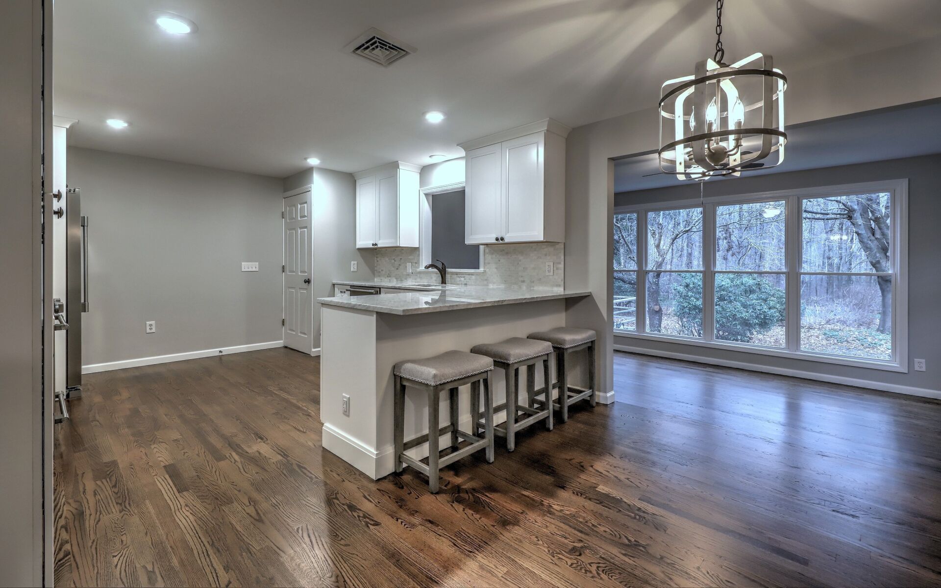 Kitchen with white cabinets, gray walls, dark wood floors, and a view of trees.