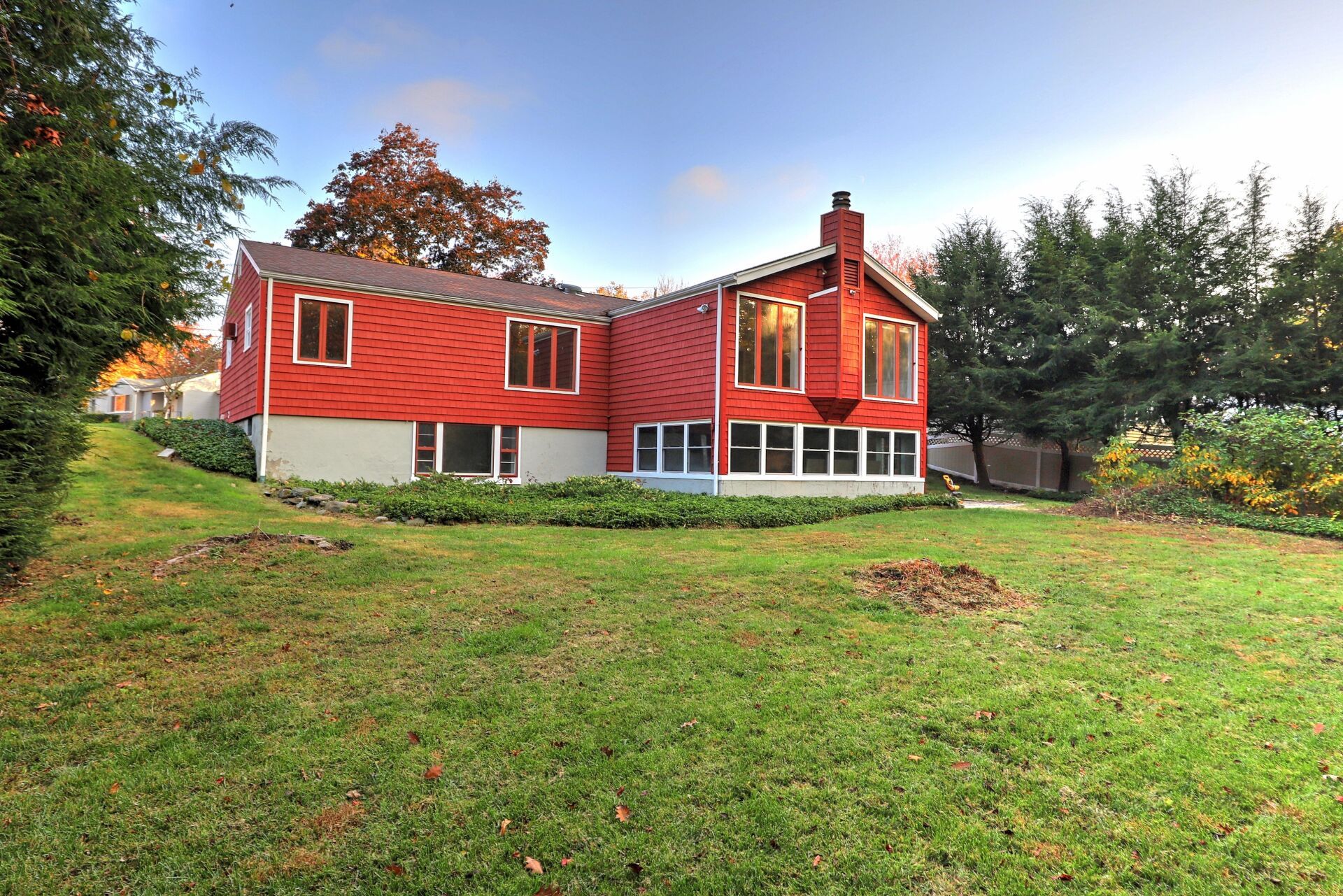Red house with a green lawn and trees under a blue sky.