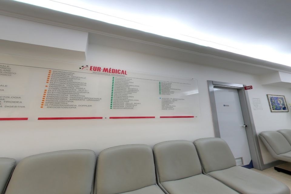 Sala d'attesa con posti a sedere, bacheca e porta in una struttura medica.