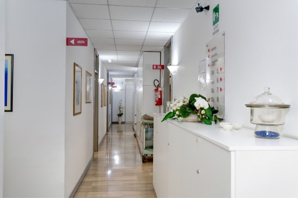 Un corridoio bianco con un bancone della reception. Una composizione floreale è posta in cima. È presente un cartello di uscita.