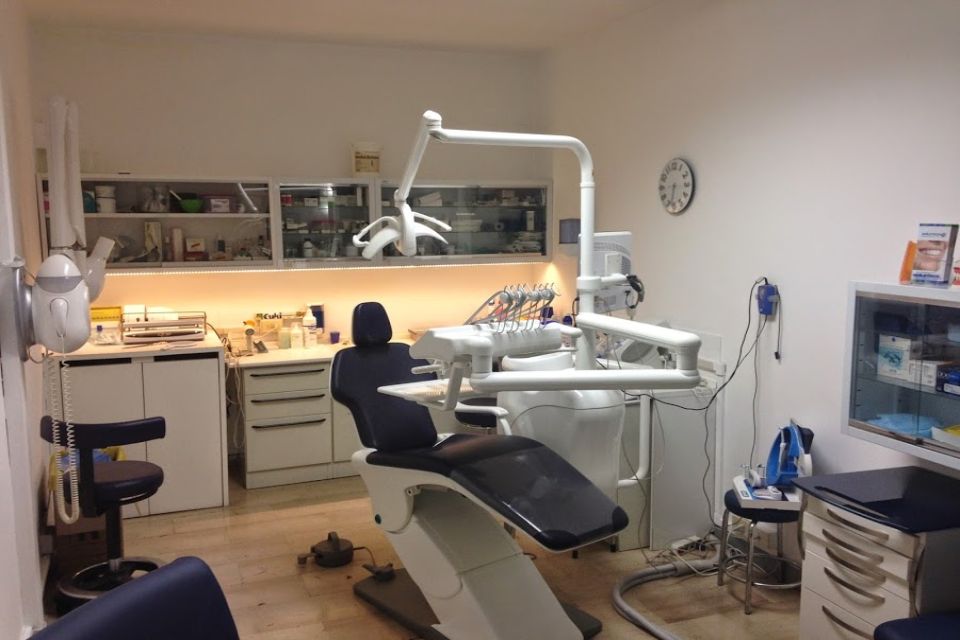 Interno di uno studio dentistico con poltrona, attrezzature e armadietti.