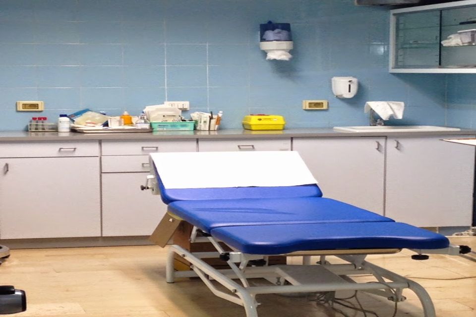 Sala visite con pareti blu, lettino medico, armadietti e lavandino.