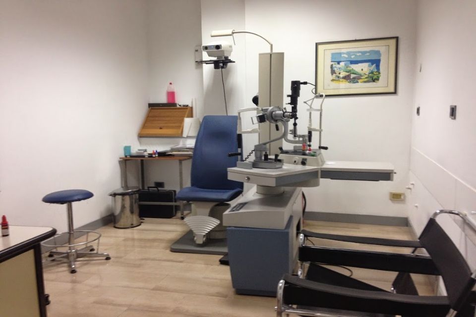 Una sala per visite oculistiche con una sedia blu, attrezzatura per visite oculistiche e uno sgabello.