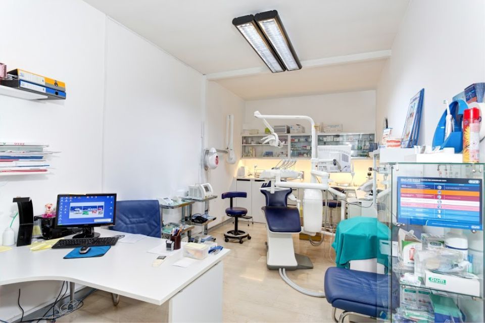 Studio dentistico con poltrona, attrezzatura, scrivania, computer. Pareti bianche e luminose.